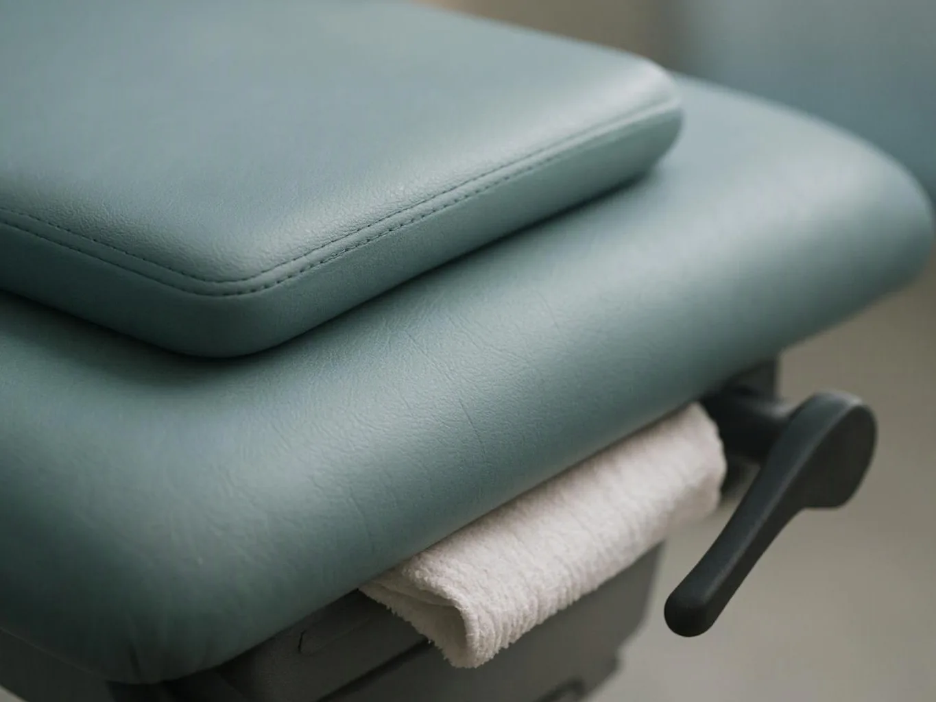Close-up of a padded medical exam table with a paper roll and black adjustment lever