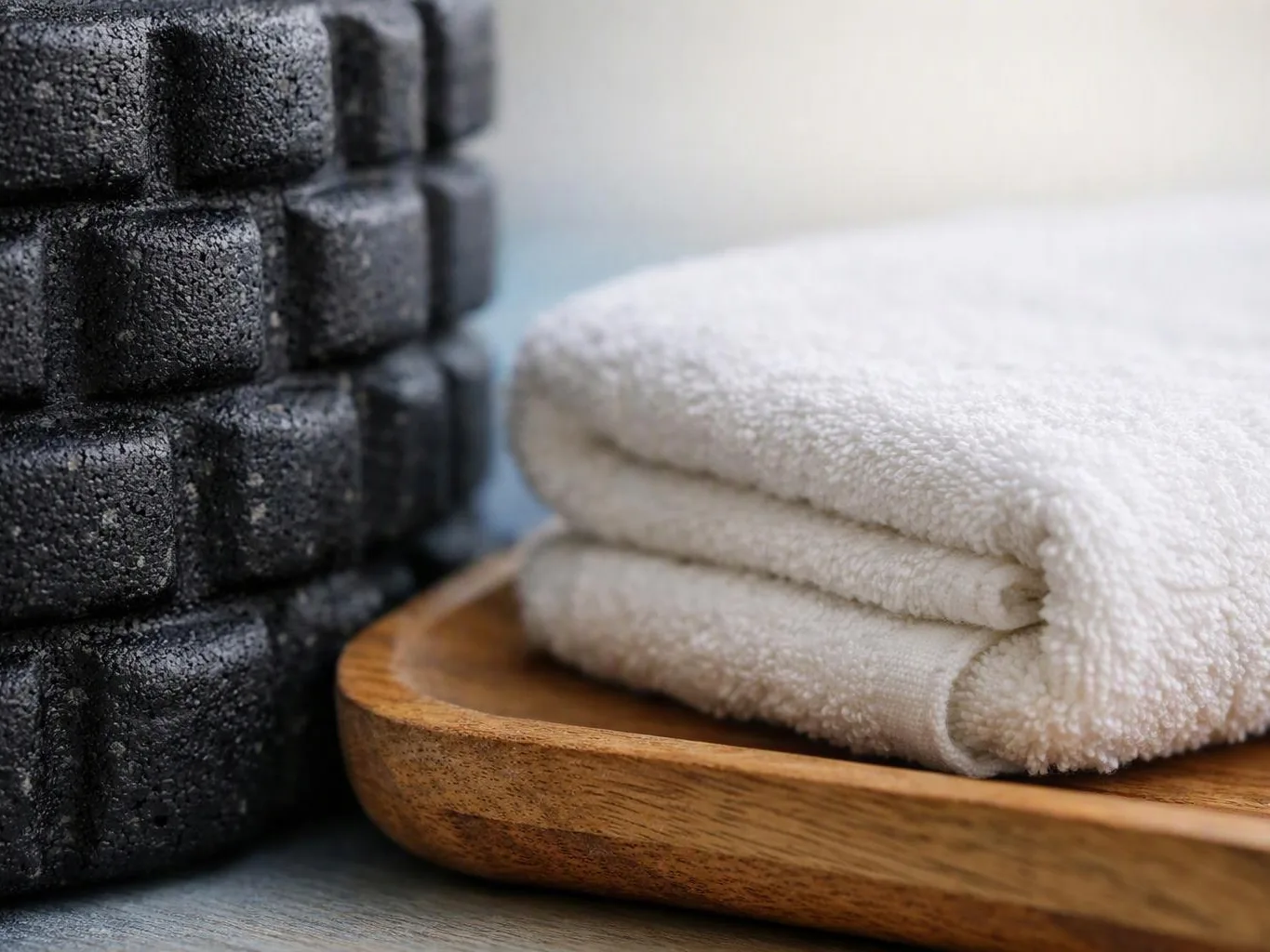 A folded white towel rests on a wooden tray beside stacked black foam rollers